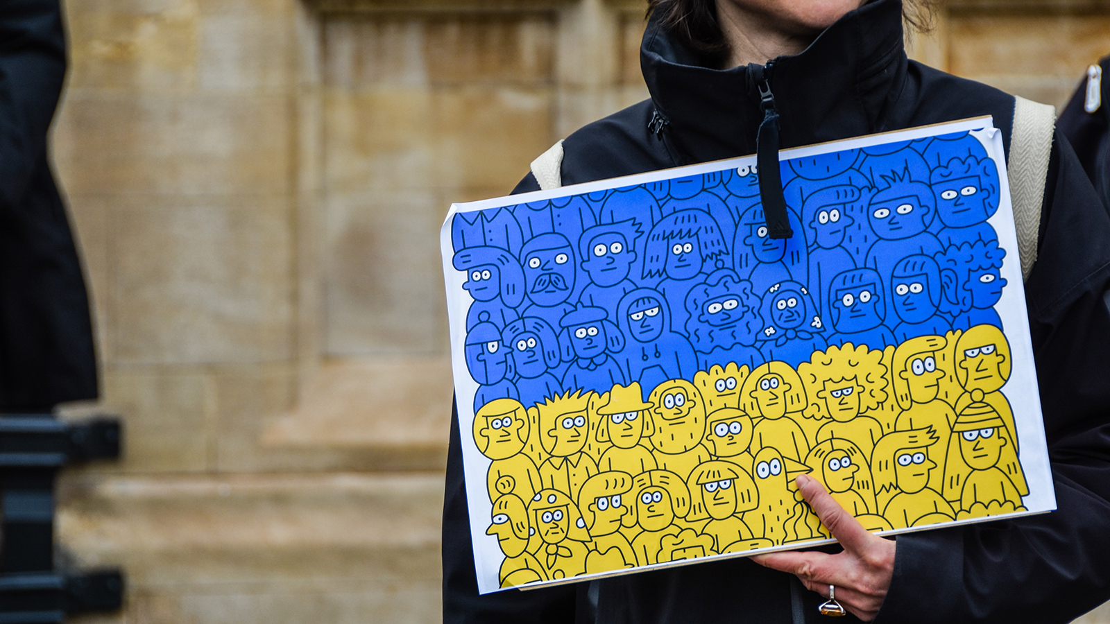A person is holding a sign in blue and yellow, reminiscent of the Ukrainian flag.